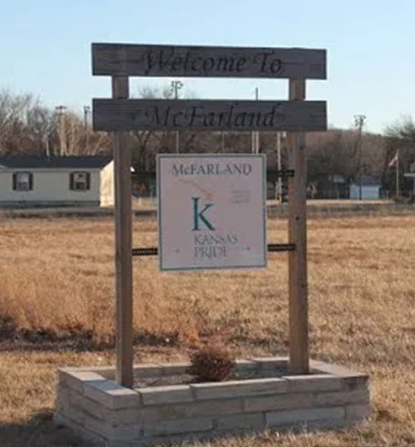 A sign in front of a field with a house and some grass.